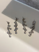 Nærbilde av Daisy Flower i sølv med blå cubic zirconia stener og et par med hvite stener, øredobbene ligger delikat på en baderomsvask.