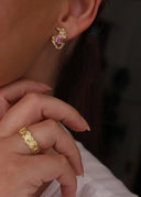 En ung kvinne med brunt hår utsmykket med Melodie øredobb i rosa og Star Wave ring i gull.