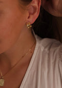 Nærbilde av en kvinne med brunt hår utsmykket med en gulløredobb med oliven farget sten i øret.