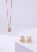 Lykkesten halskjede med rosa cubic zirconia sten og matchende melodie øredobber med rosa stein er plassert på en delikat hvit bakgrunn.